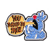 A lapel pin featuring a stylized blue creature with a red eye and text that reads You Turned the Page!