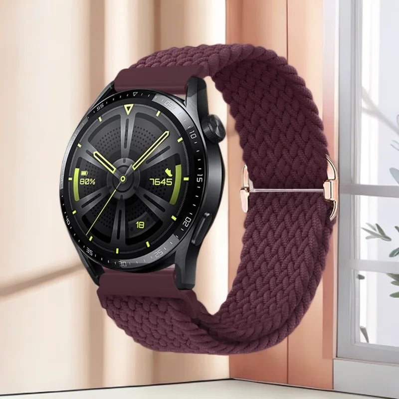 A black smartwatch face is shown on a deep purple knitted nylon watch strap next to a window.