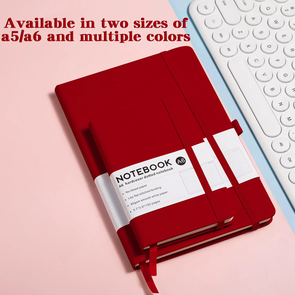 A red hardcover notebook with a white cover and spine is shown next to a white keyboard.