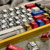 A collection of colorful comic style mechanical keycaps arranged in a yellow tray.