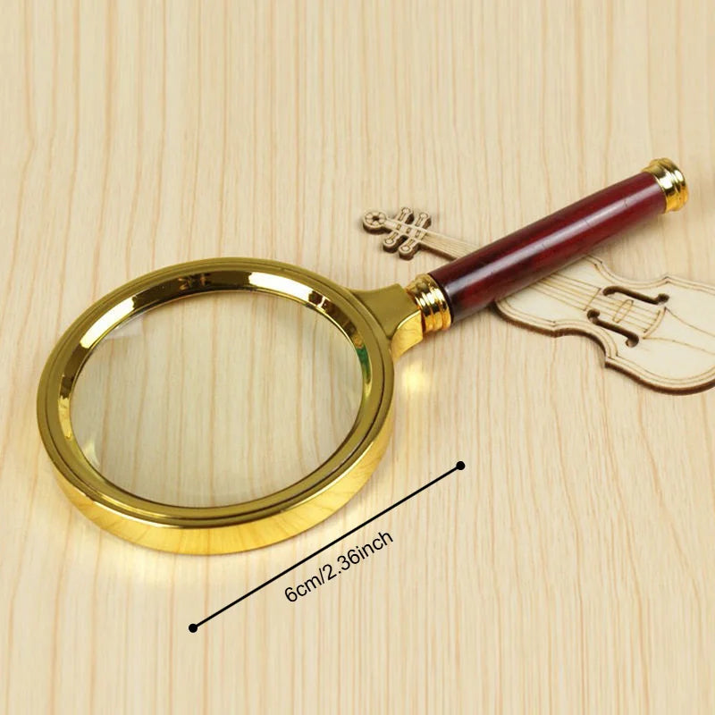 A gold-rimmed magnifying glass with a wooden handle rests on a light wood surface.