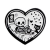A heart-shaped enamel lapel pin featuring a skull and book design with stars and a cat silhouette.