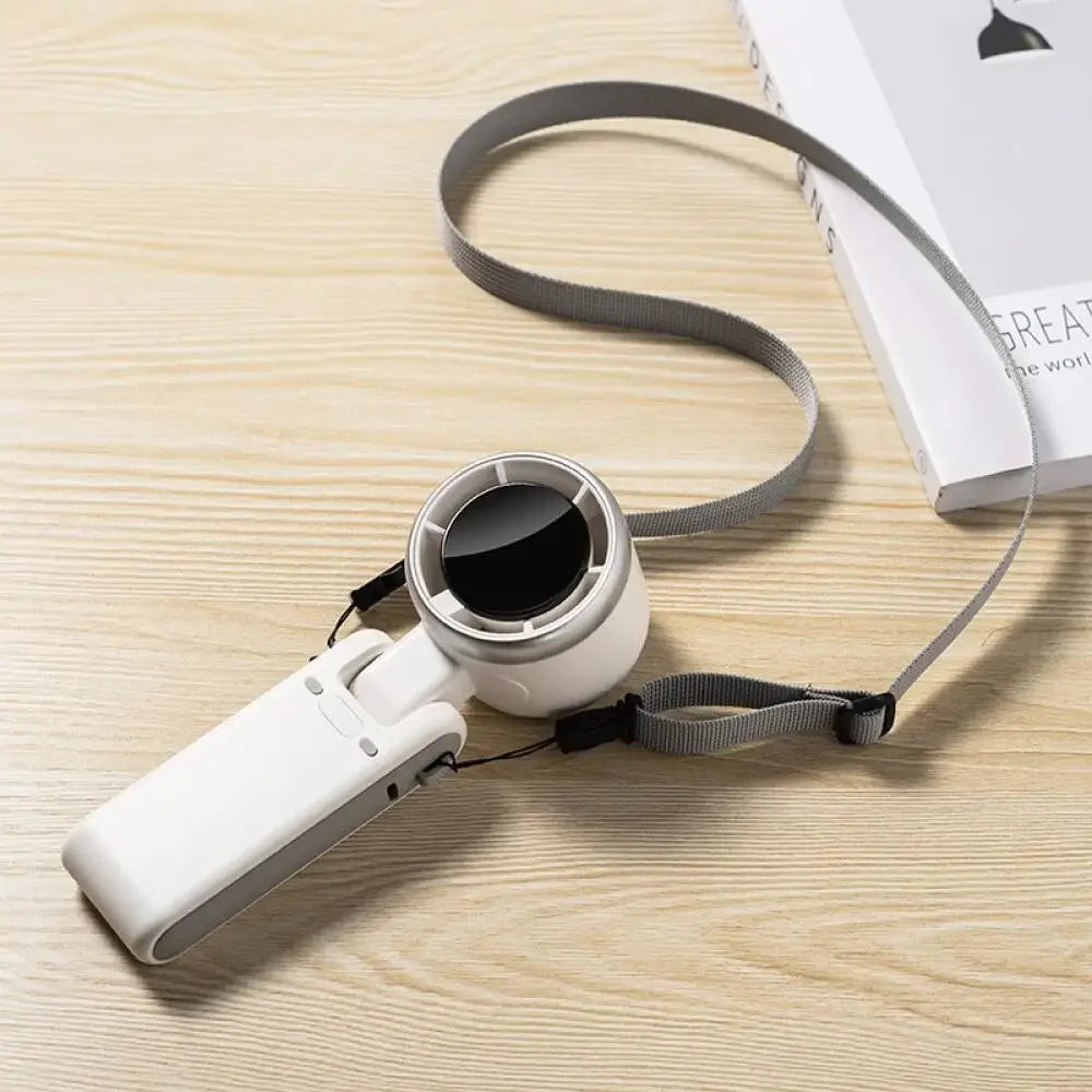 Weißer, faltbarer, wiederaufladbarer USB-Handventilator mit schwarzem Gitter und grauem Riemen auf Holzoberfläche.