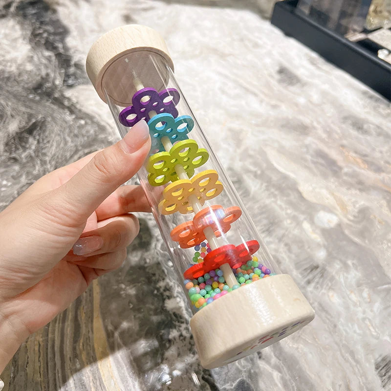 A hand holds a wooden rain sound tube musical instrument filled with colorful plastic beads.