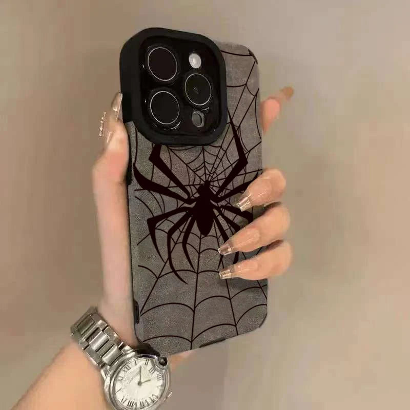 A hand holds a gray phone case featuring a black spider web design, next to a silver wristwatch.