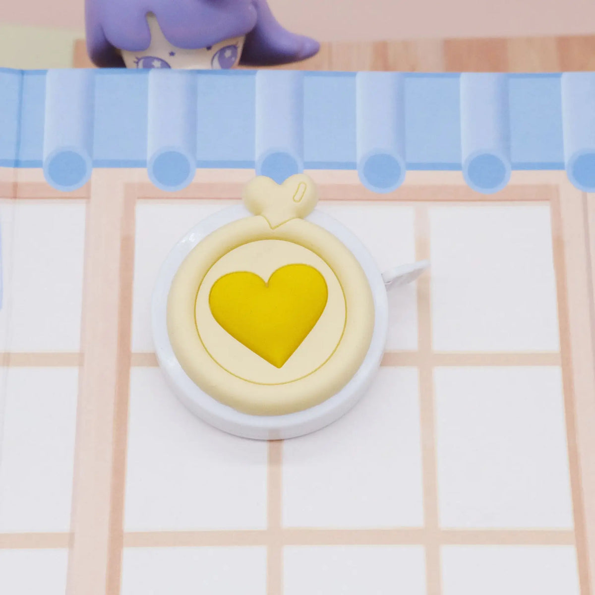 Un objeto en forma de corazón amarillo colocado sobre una herramienta de medición blanca contra un fondo rosa claro.