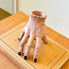 A light pink resin palm hand decoration with black accents resting on a brown book.