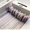 A roll of purple washi tape thin in a box, with several rolls displayed on a sheet showing various patterns.