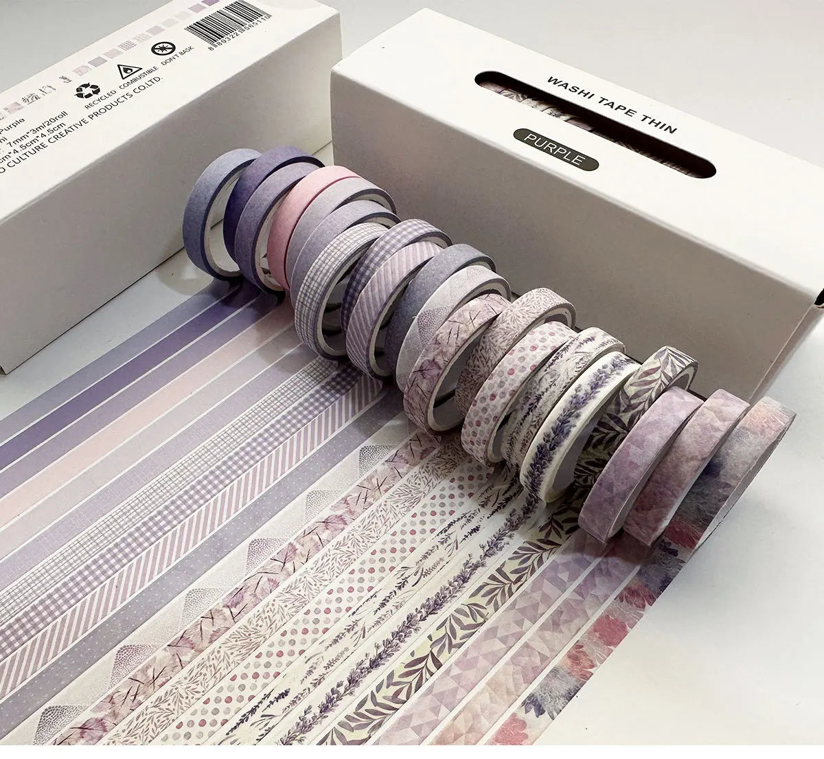 A roll of purple washi tape thin in a box, with several rolls displayed on a sheet showing various patterns.