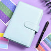 A light blue A6 budget planner with a leather cover and envelope system resting on a purple surface.