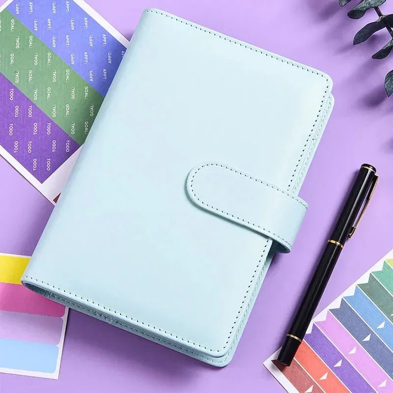 Planificador de cuero PU azul claro A6 en una superficie morada junto a papel colorido.