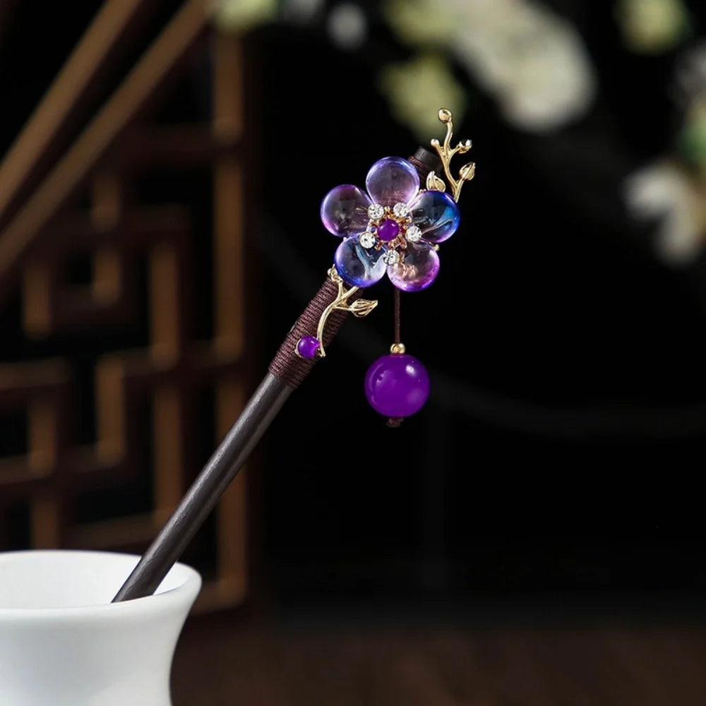 Une épingle avec un bâton en bois foncé et un accessoire de fleur en verre violet avec des accents dorés.