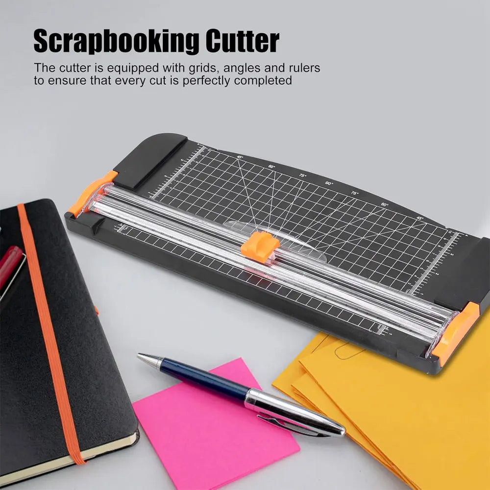 Herramienta de corte para scrapbooking negra con riel deslizante y cuadrículas, junto a un cuaderno y papel de colores.