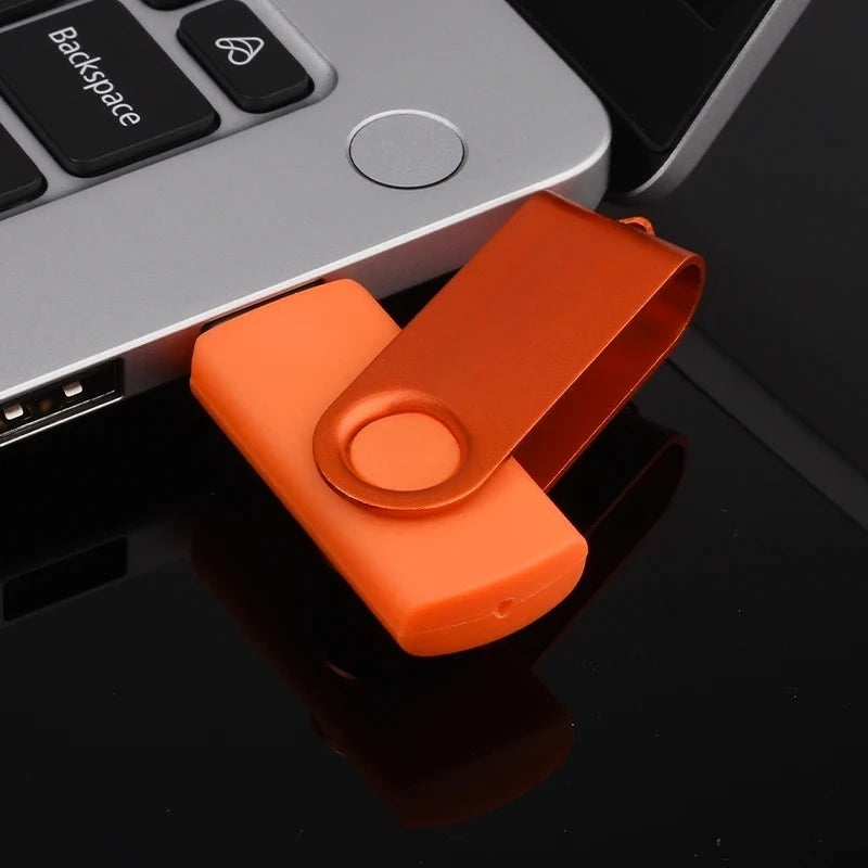 Ein orange, drehbarer Metall-USB-Stick liegt auf einer dunklen Oberfläche neben einem silbernen Gerät.