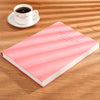 Pink notebook lying on a wooden surface next to a white cup and saucer.
