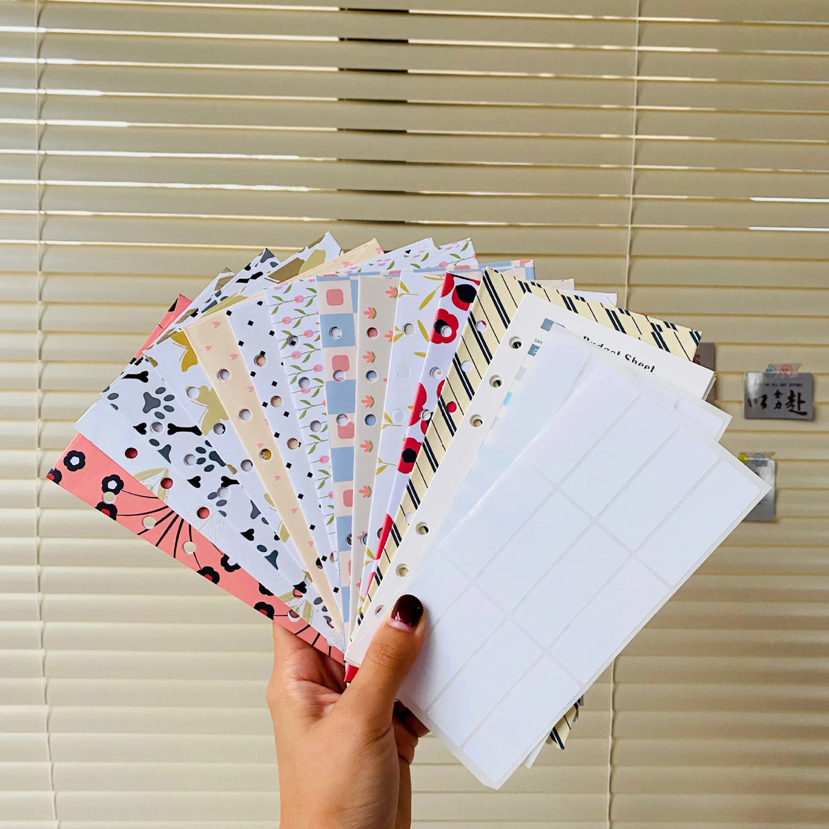 A stack of A6 budget planner binders with envelope pockets and expense sheets displayed against a light wood slat background.
