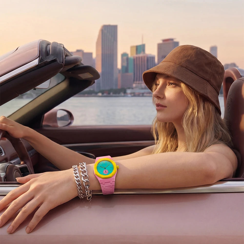 A woman wearing a brown hat and gold bracelets rests her arm on the door frame of a car, displaying a pink ceramic watch.