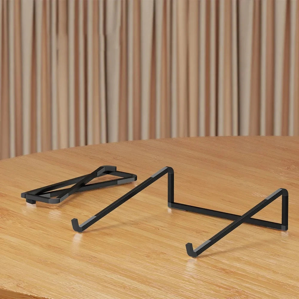A black foldable aluminum laptop stand with non-slip grips resting on a wooden surface.