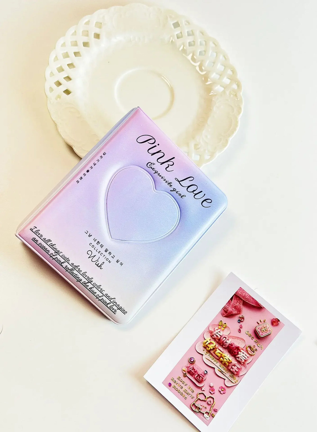A pink heart-shaped photo card binder for Kpop albums resting on a white plate.