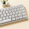 A close-up of a white mechanical keyboard with light gray keycaps and a small white rabbit in the background.