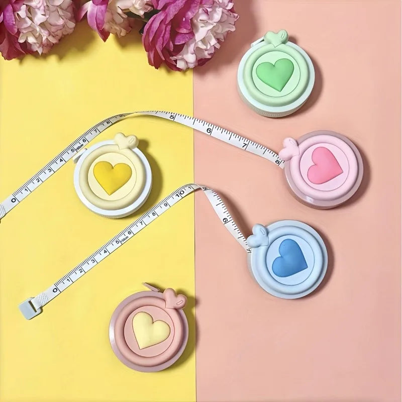 Una cinta métrica corazón retráctil y compacta con corazones de varios colores, mostrada sobre un fondo rosa y amarillo.