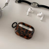 A tortoiseshell patterned protective case for AirPods rests next to a black watch and white wireless earbuds.