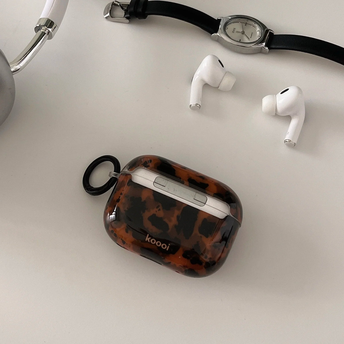 A tortoiseshell patterned protective case for AirPods rests next to a black watch and white wireless earbuds.