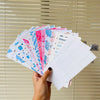 A hand holds a stack of A6 budget planner binders with envelope pockets and expense sheets.