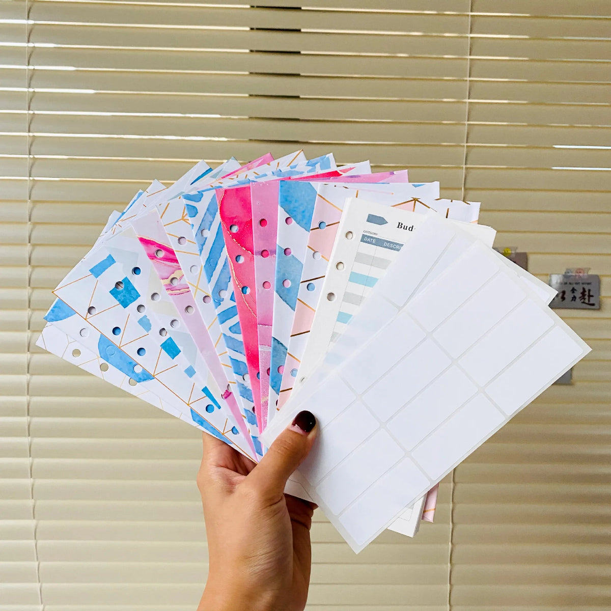 A hand holds a stack of A6 budget planner binders with envelope pockets and expense sheets.