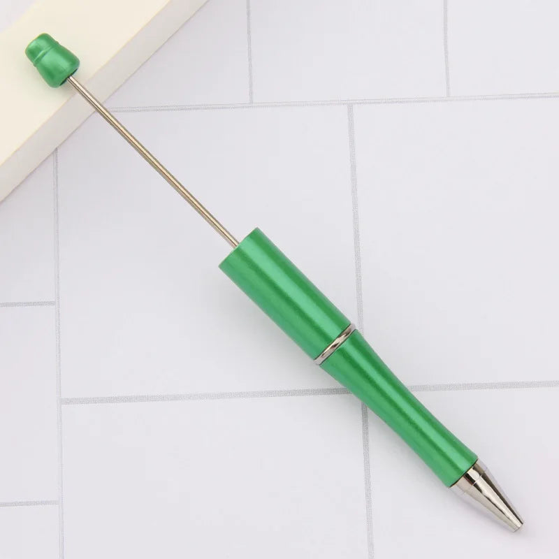 A green DIY beadable pen with a silver tip is shown resting on a white surface.
