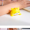 A yellow cat-shaped ergonomic wrist rest is placed on a white desk next to a hand using a computer.