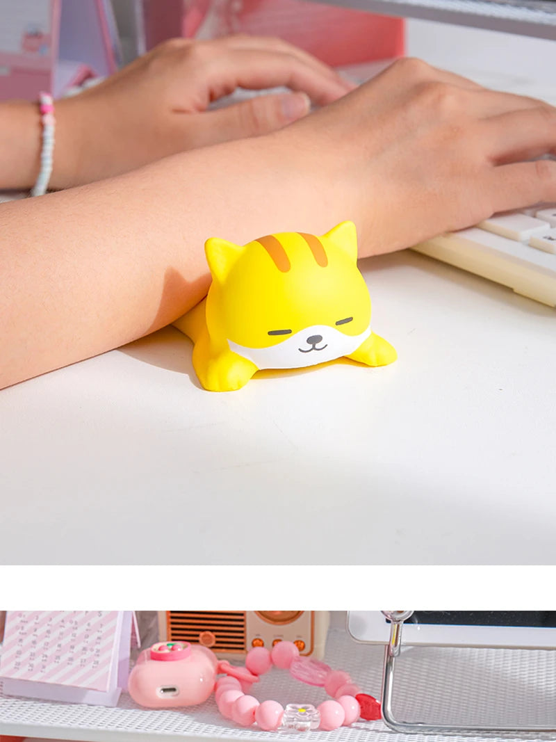 A yellow cat-shaped ergonomic wrist rest is placed on a white desk next to a hand using a computer.