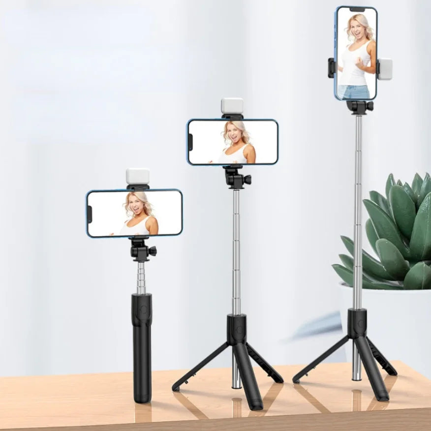 A silver selfie stick tripod with a smartphone mounted on top, featuring a fill light and wireless remote.