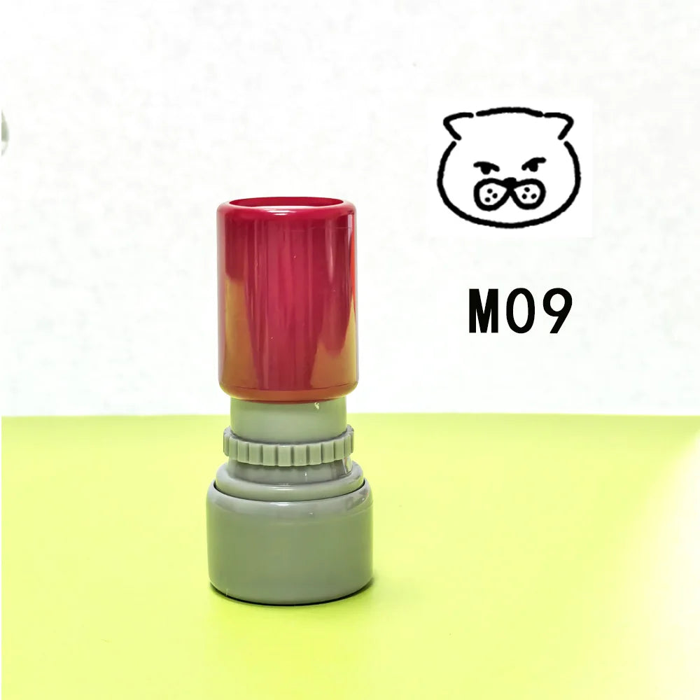 A red and gray teacher stamp with a cat face design is shown on a yellow surface.