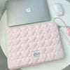 A pink quilted laptop sleeve with a white gingham pattern rests on a white table next to an Apple laptop and mouse.
