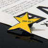 A yellow star enamel pin with the text your did it is placed on a dark surface.