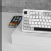 Teclado de juego silencioso MageGee GK950 blanco con cable, mostrado sobre una superficie blanca junto a un smartphone.