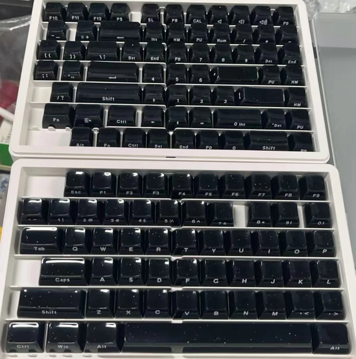 A close-up view of a white plastic case containing custom printed black jelly keycaps for mechanical keyboards.