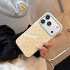 A hand holds a light yellow phone case with white polka dots and a clear ring, next to a gray hat.