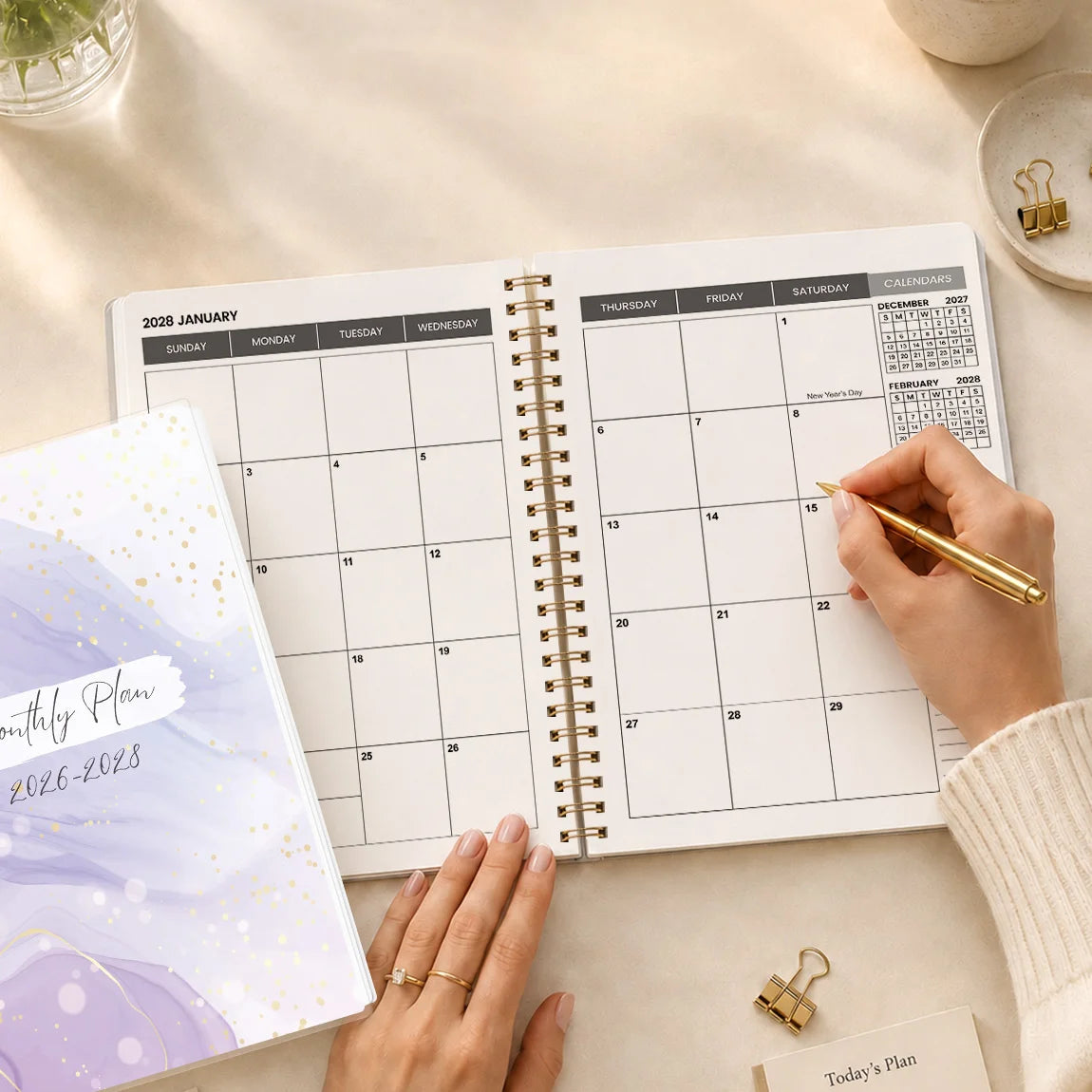 A close-up of an A5 monthly planner with a purple marble design and gold spiral binding, showing a handwritten plan.