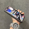 A hand holds a dark gray phone case with a silver watch on the wrist.