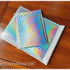 A stack of iridescent rainbow foil bubble mailers for gifts and documents resting on a wooden surface.