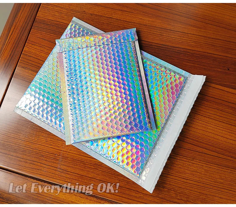 A stack of iridescent rainbow foil bubble mailers for gifts and documents resting on a wooden surface.
