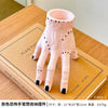 Pink resin palm hand decoration with black accents displayed on a cardboard box.