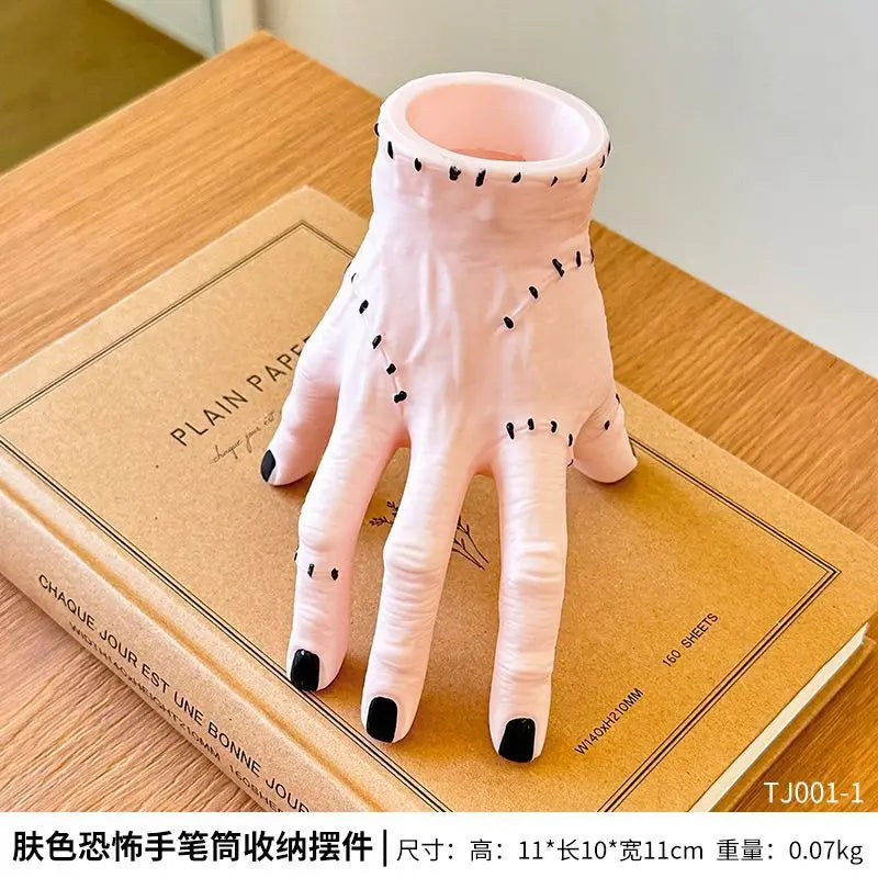 Pink resin palm hand decoration with black accents displayed on a cardboard box.