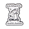 An enamel pin featuring a frog riding a bicycle with the text It Is What It Is And It's Autism