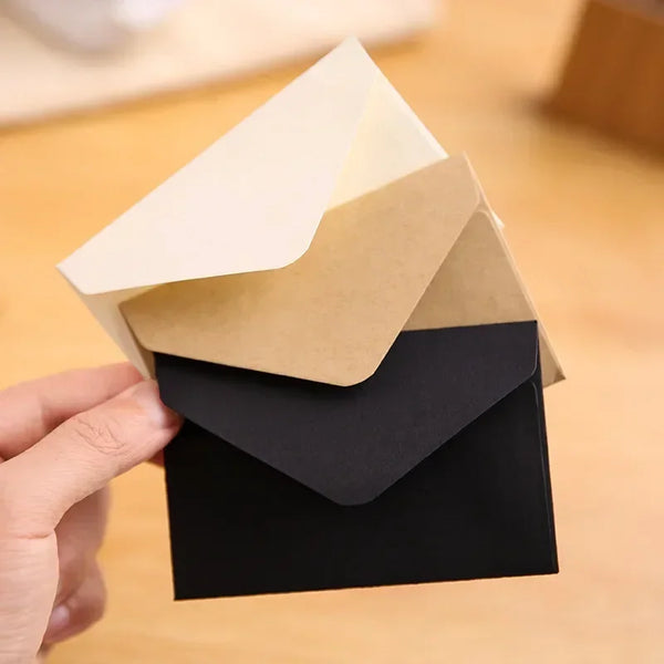 A hand holds a stack of kraft paper wedding invitation envelopes in various shades of beige and black.