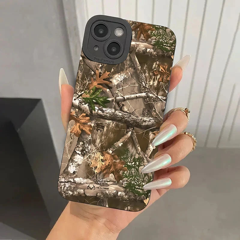 Une main tient une coque de téléphone à motif camouflage de forêt avec des branches et des feuilles.
