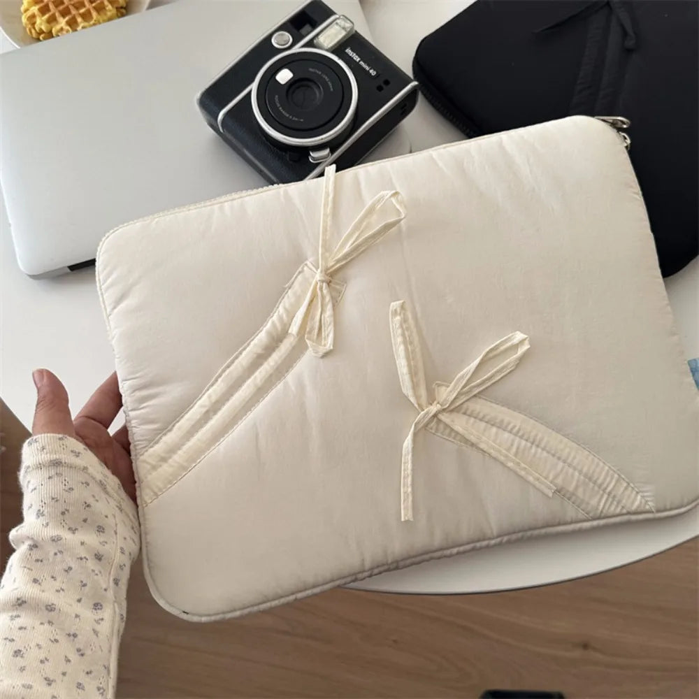A beige ultra-thin laptop sleeve case is shown next to a camera and on a white surface.