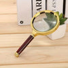 A gold-framed magnifying glass with a dark handle rests on a wooden surface next to a stack of books.